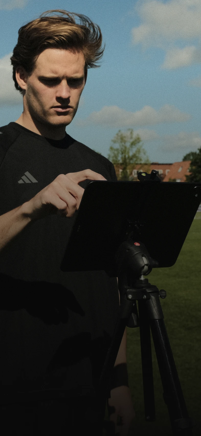 A person in a black shirt using a tablet on a tripod outside on a sunny day with a blue sky and clouds in the background.