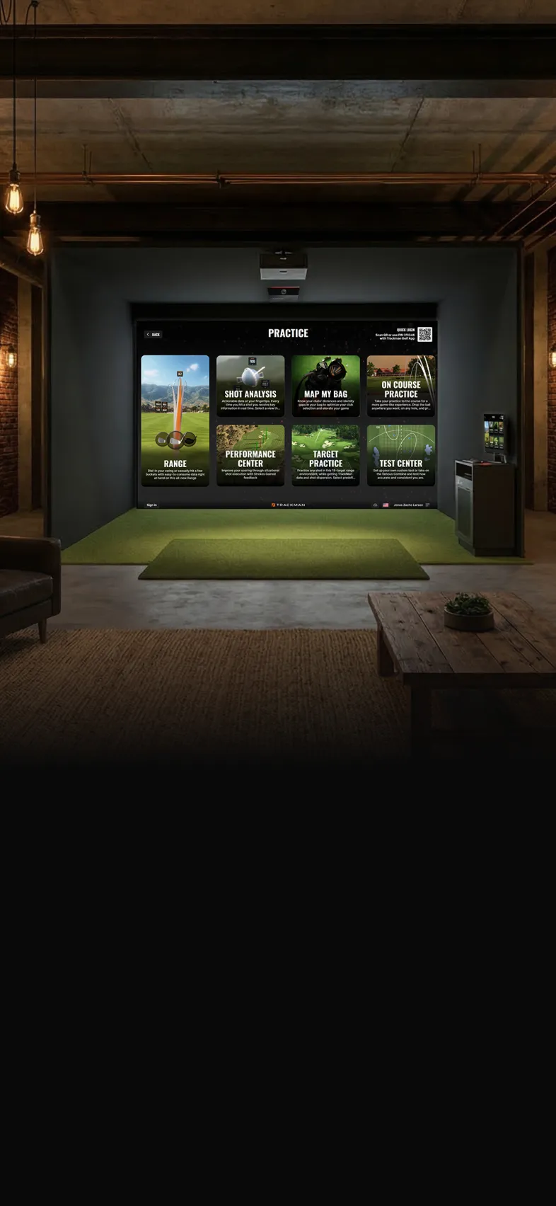 A modern golf simulation room with a large screen displaying various practice options, a mat, and cozy seating in a dimly lit space.
