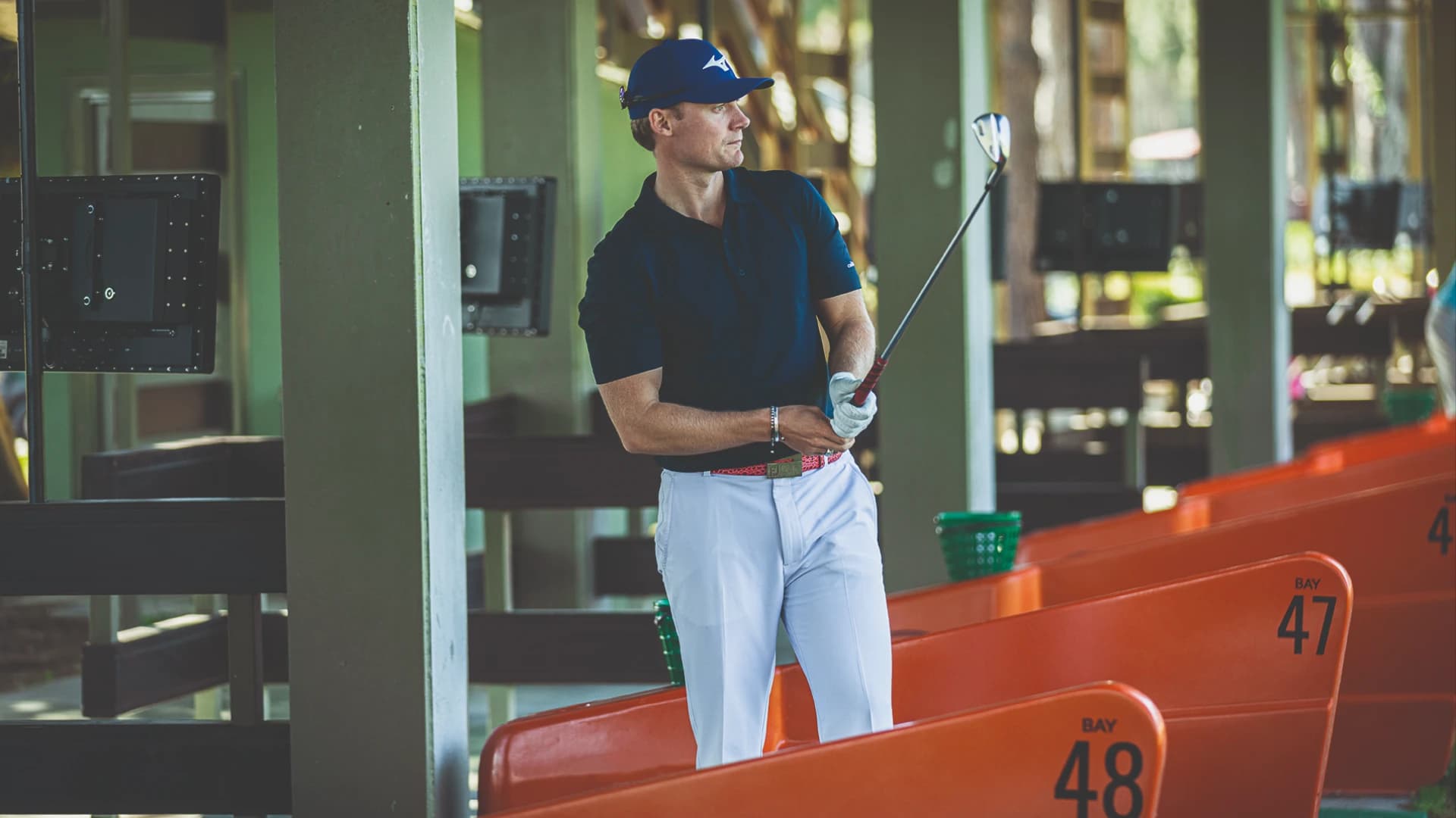 Golfer in blue cap and shirt practicing at a driving range, holding a club near bays numbered 47 and 48.